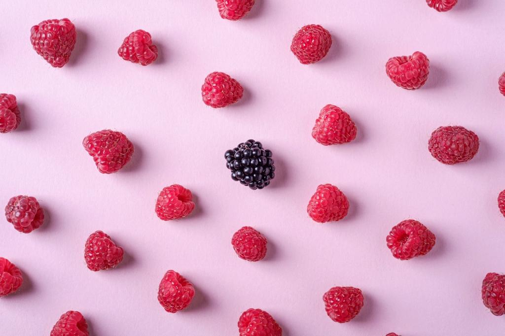 Einzeln in Reihen aufgelegte Himbeeren mit einer Brombeere in der Mitte auf rosa Untergrund.