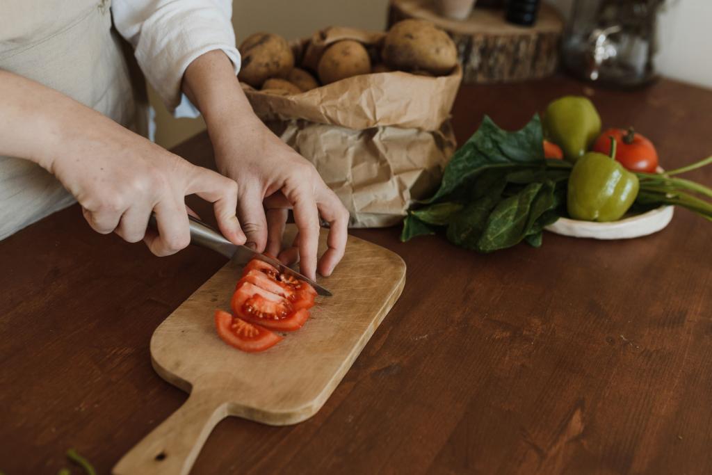 Hände, die auf einem hölzernen Schneidebrett eine Tomate in Stücke schneiden. 